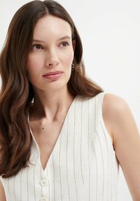 Witte, gestreepte mouwloze blouse met een V-hals en drie knopen aan de voorkant. Gladde textuur, getailleerde pasvorm, minimalistisch ontwerp.