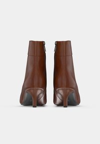 Pari ruskeih nahast gležnjačev s stranskimi zadrgami in srednje visokimi petami, prikazanih s hrbtne strani na enobarvni beli podlagi.