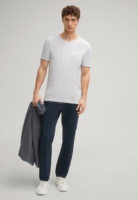 Lichtgrijze katoenen t-shirt, marineblauwe broek, houdt een donkergroene trui vast. Witte sneakers maken de outfit compleet, met een relaxte pasvorm en een minimalistisch ontwerp.