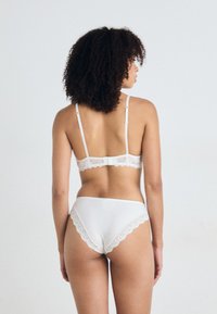 Witte beha en bijpassende slip met kanten rand. De beha heeft verstelbare bandjes en een haaksluiting; de stof is glad met een lichte glans.