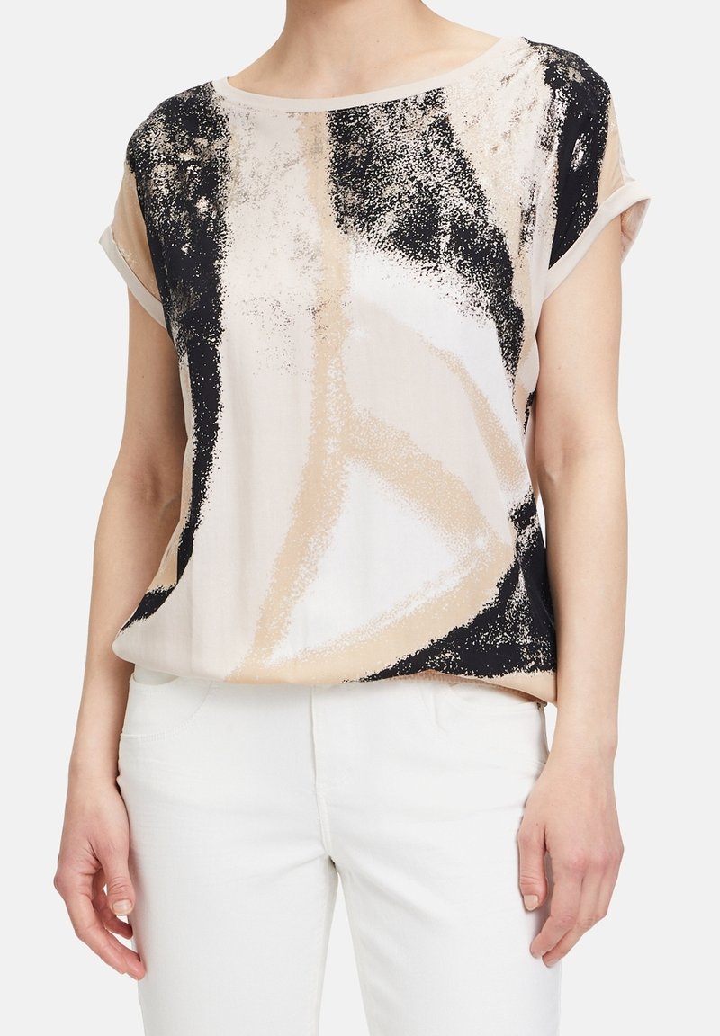 Bluzka krótki rękaw z lekkiego materiału, w beżowym tle z czarnymi i ciemnobrązowymi abstrakcyjnymi wzorami. Lekko luźny krój.