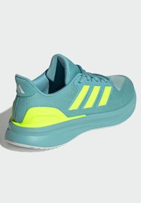 Zapatilla deportiva en color verde azulado con acentos en amarillo neón, parte superior de malla, suela texturizada y logotipo de tres rayas en el costado. Diseño de talón curvado.