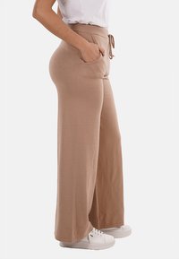 Pantaloni beige a gamba larga con vita elastica, dettagli con cordino e tasche laterali. Realizzati in morbido tessuto testurizzato, abbinati a sneaker bianche.