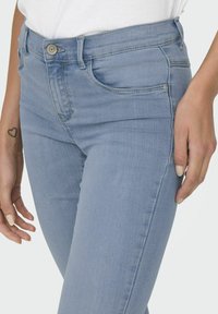 Jeans de mezclilla azul claro con un diseño ajustado, que cuentan con un estilo clásico de cinco bolsillos, pasadores para cinturón y una textura ligeramente desgastada.