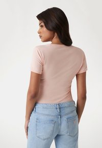 Lys pink fitted t-shirt med korte ærmer, parret med lyseblå højafrettede jeans med baglommer og en lille logo detalje.