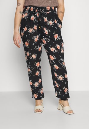 Zwarte ontspannen broek met roze en perzikkleurige bloemenprint, trekkoord in de taille, gedragen met beige open-toe sandalen met blokhak en een bruin topje.