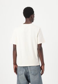 Cremefarvet bomulds-T-shirt med afslappet pasform, korte ærmer og rund halsudskæring, parret med lyseblå denimjeans.