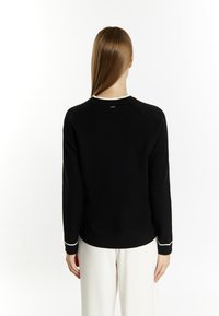 Schwarzer Pullover mit langen Ärmeln und rundem Ausschnitt, der weiße Akzente an den Ärmelbündchen aufweist. Glatte Textur, lässige Passform und Raglanärmel.