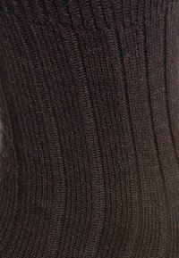 Tejido de lana negra de punto con una textura acanalada; presenta líneas verticales alternas y una apariencia suave y peluda.