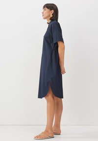 Navy Baumwollhemdkleid mit kurzen Ärmeln, seitlichen Schlitzen und elastischem Bund. Verfügt über eine einzelne Brusttasche und ein minimalistisches Design.