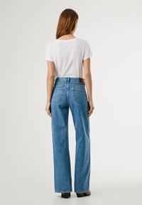 T-shirt bianca leggera a maniche corte abbinata a jeans a vita alta di un blu chiaro con gamba larga, con tasche posteriori e dettaglio in pelle.