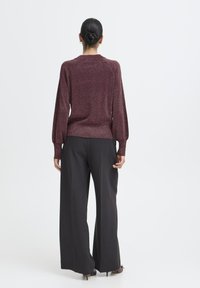 Bordowy metaliczny sweter o luźnym kroju i bufiastych rękawach, zestawiony z wysokimi czarnymi spodniami o szerokich nogawkach. Gładka tekstura i prosty design.