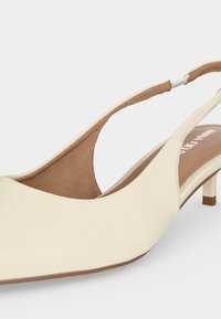 Κρεμ παπούτσι χαμηλού τακουνιού με λουρί πίσω και μυτερή μύτη, ελαστικό λουράκι, με λείο δερματοειδές επάνω μέρος και καφετί εσωτερική επένδυση.