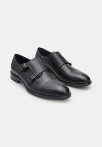 Zapatos de vestir de cuero negro con doble tira de monk, textura suave, puntera puntiaguda y un tacón bajo y sólido. Los detalles incluyen hebillas.