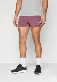Shorts de sport pour hommes en tissu bourgogne foncé, légers, présentant une texture lisse. Associés à des chaussures de course noires et des chaussettes blanches.