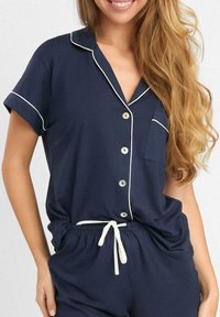 Granatowy zestaw piżamowy z krótkimi rękawami, białym wykończeniem, zapięciem na guziki i kieszenią na piersi. Elastyczny pasek w talii z trokiem. Miękka tekstura materiału.