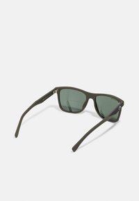 Óculos de sol com tonalidade verde, com uma armação mate na cor azeitona, lentes em forma quadrada e hastes delgadas com um detalhe texturizado.