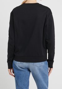 Sudadera negra con cuello redondo, mangas largas y puños y dobladillo acanalados. La vista posterior muestra una textura lisa y un ajuste relajado.