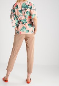Blusa floreale rosa con foglie verdi, abbinata a pantaloni beige e sandali rossi. Presenta una vestibilità ampia e una silhouette rilassata.