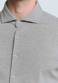 Graues Polohemd mit strukturiertem Finish, klassischem Kragen und drei Knöpfen auf der Vorderseite. Das Material ist weich und leicht.