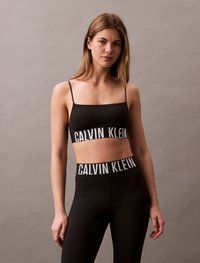 Top cropped preto com alças finas e uma faixa com o logótipo "CALVIN KLEIN" em branco, combinado com leggins pretas de cintura alta com a mesma faixa do logótipo.