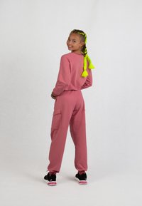 Rosa Sweatshirt und passende Jogginghose aus weichem Material, mit langen Ärmeln, gerippten Bündchen und Taschendetails. Schwarze Sneaker mit pinken Akzenten.