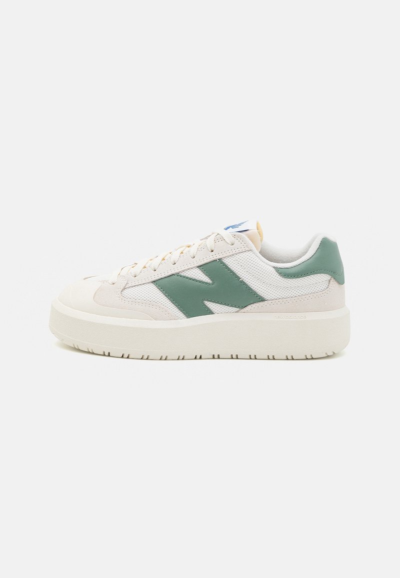Baskets basses avec dessus en mesh beige et blanc, logo latéral en cuir vert, semelle épaisse blanche et lacets beiges sur fond uni.