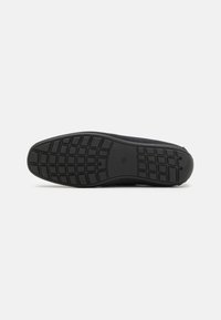 Semelle de sneaker noire avec un motif en caoutchouc texturé. Contient des rainures et des formes pour l'adhérence. Design minimaliste avec un bout arrondi.