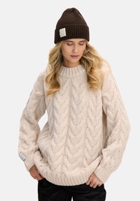 Kość słoniowa sweter z grubym splotem, z wysokim kołnierzem, szerokimi rękawami i prążkowanym dołem. W połączeniu z ciemnobrązową prążkowaną czapką beanie.