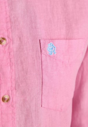 Rosa Leinenhemdtasche mit kleinem blau besticktem Logo und beigen Knöpfen entlang der vorderen Knopfleiste.