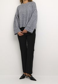 Grå oversize tröja med texturerad stickning, kort längd och vida ärmar, kombinerad med svarta skräddarsydda byxor och spetsiga svarta skor.