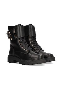 Botas cortas de cuero negro estilo militar con puntera inclinada, cordones en la parte delantera y dos detalles decorativos de hebilla en el lateral. Suela de goma gruesa.