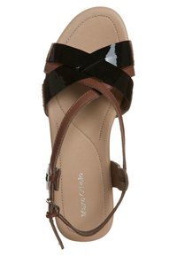 Tige en cuir verni noir avec des brides en cuir marron. Semelle plate avec un design de bride croisée. Marquage argenté sur le côté intérieur.