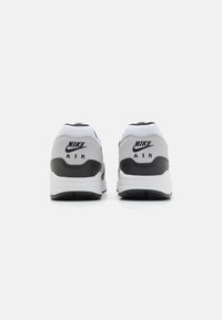 Nike Air sneakers featuring a white and gray upper, black heel accents, and textured materials. Includes distinct branding on the heel.
