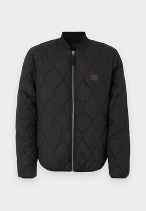Veste bomber matelassée noire avec un col côtelé ; comporte une fermeture éclair à l'avant et un petit patch logo sur la poitrine gauche. Texture douce.