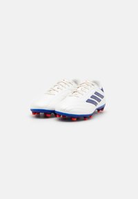 Scarpe da calcio bianche con tre strisce blu, suola rossa con tacchetti e design testurizzato. Presentano lacci beige e colletto imbottito.