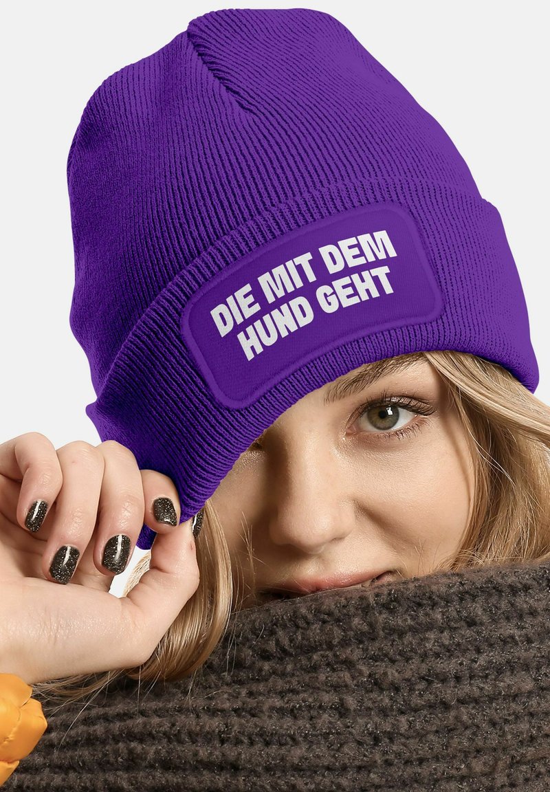 Purple knit beanie with a textured finish and a rectangular patch displaying white text. Soft material visible around the edges.