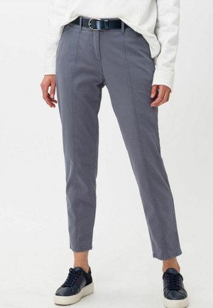 Person iført grå slim-fit bukser, sort bælte, hvid skjorte med lange ærmer og marineblå sneakers med hvide såler.