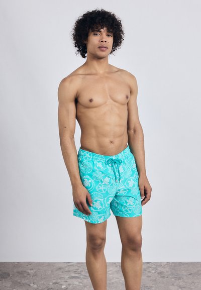 Turkizne kopalne hlače z belimi vzorci školjk in želv, z elastičnim pasom in vrvico, narejene iz lahkega materiala.