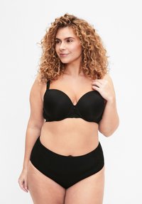 Soutien-gorge noir rembourré avec armatures, texture lisse, bretelles ajustables et un fermoir décoratif au centre. Associé à un slip noir taille haute avec des accents en dentelle.