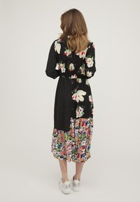Květinové midi šaty s černými puntíky a květinovým patchworkovým designem, vrstvený volánkový lem a stažený pas. Spárováno s bílými teniskami.