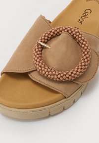 Sandalo in suede marrone chiaro con una fascia ampia, un accento di perline circolari in un delicato rosa e una suola in gomma testurizzata con un motivo in rilievo.
