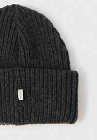 Pletená čiapka tmavosivej farby s vertikálnou rebrovanou textúrou. Mäkký materiál z vlny. Na boku je malá štítok s logom značky.