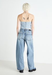 Denim majica s strukturiranim korzetom, v kombinaciji z ohlapnimi, svetlo modrimi kavbojkami. Črne debele škornje dopolnjujejo oblačilo. Zadnji pogled na model.