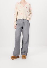 Beige kofta med rosa hjärtmönster, v-ringning och knäppning, i kombination med lösa grå jeans och bruna mockastövlar med plattform.