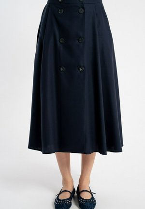 Granatowa spódnica midi z podwójnym rzędem guzików w kształcie kotwicy, noszona z granatowymi plecionymi balerinami Mary Jane, pokazana od talii do stóp.