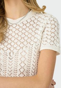 Suéter blanco de punto con mangas cortas que presenta un patrón de diamantes abierto, cuello y puños acanalados, con un acabado suave y texturizado.