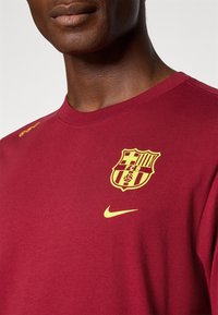 Bordeau sweatshirt, mis on valmistatud pehmest puuvillast; esiküljel on kollane Barcelona logo ja Nike swoosh. Ümmargune kaelus ja soonikkoes mansetid.