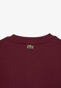 Felpa bordeaux con collo a girocollo a coste, caratterizzata da un piccolo logo di coccodrillo ricamato in verde sulla parte posteriore. Realizzata in morbido materiale tessile.