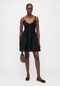 Vestido negro con un body de punto ajustado y falda acampanada, combinado con zapatos planos negros y un bolso verde oliva. Diseño sencillo, sin patrones.